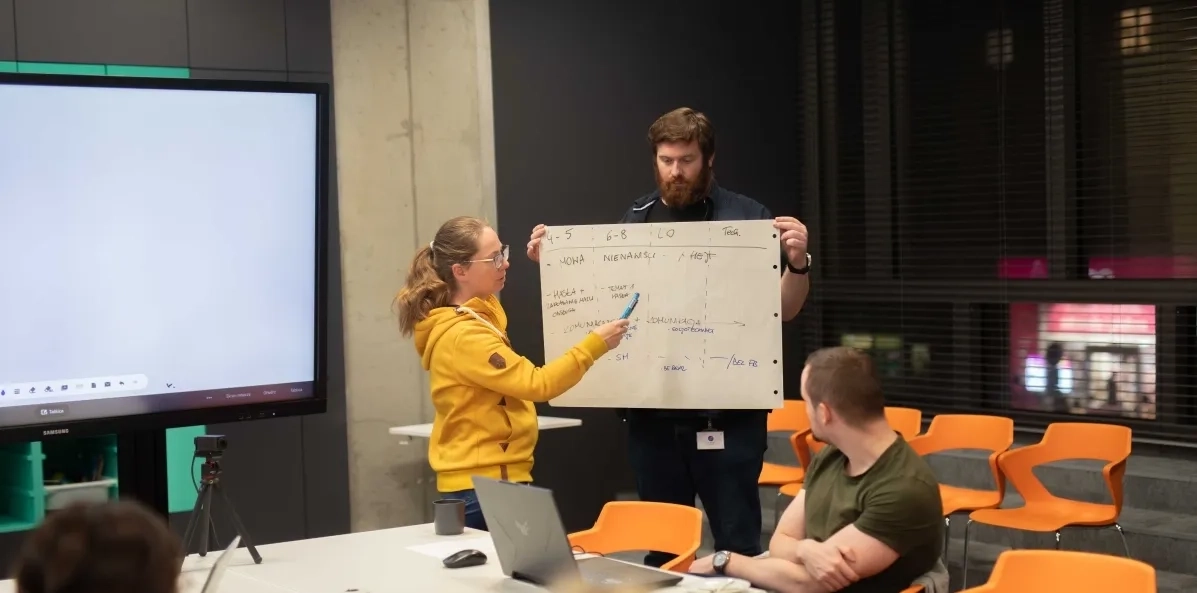 Zdjęcie przedstawiające Trenerów CDT podczas prowadzenia szkolenia. Trenerka pokazuje i objaśnia treść zapisanego flipchartu, trzymanego przez drugą osobę.